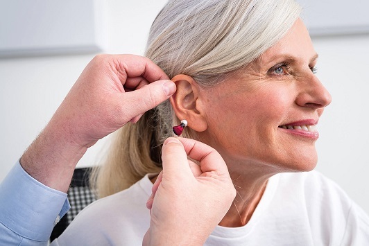 Seniorin bekommt von einem Hörakustiker ein modernes Hörgerät ins Ohr eingesetzt.